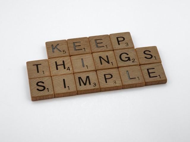 Brown wooden block on a white table saying: "keep things simple".