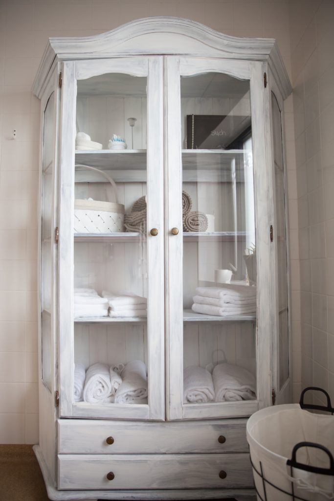 White china cabinet with glass doors containing towels. 