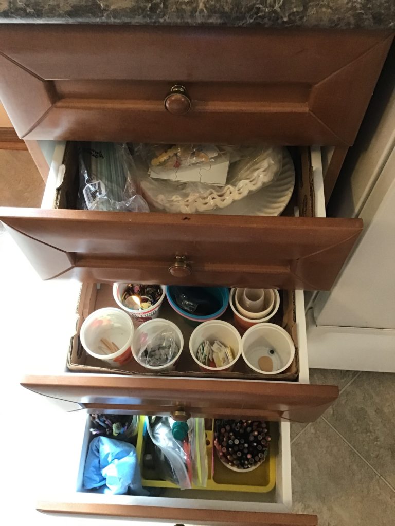 Three drawers in a kitchen each holding craft and drawing supplies for children.