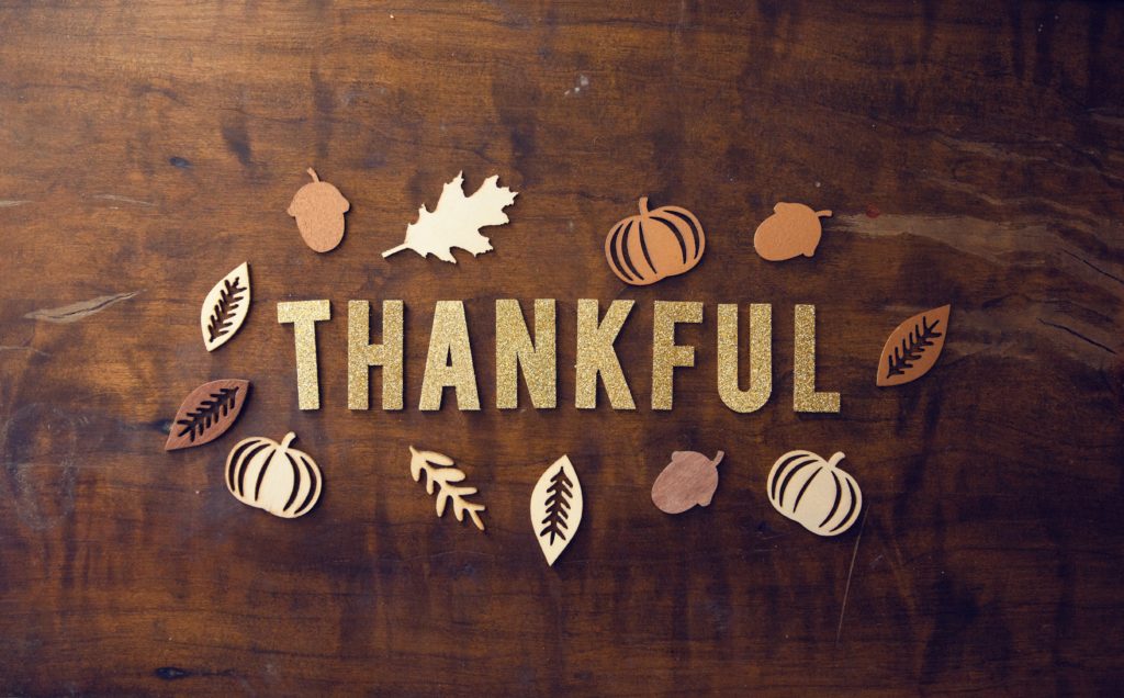 A wooden background with leaves surrounding the word thankful. 