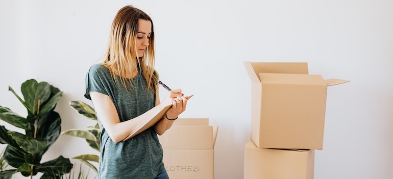 Woman making a decluttering checklist surrounded by boxes.