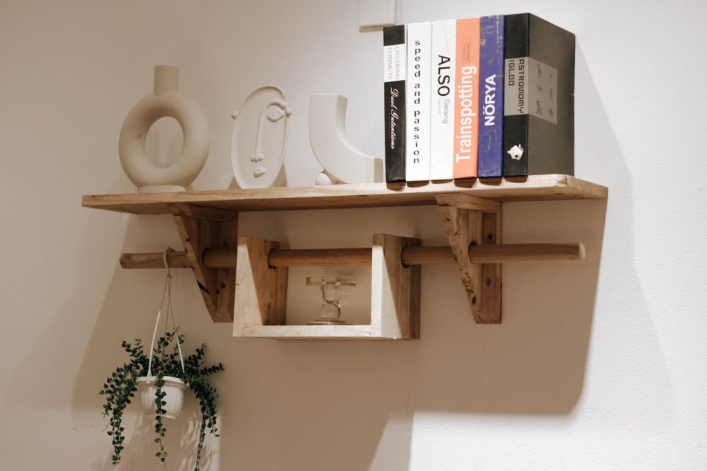 A wooden shelf with books on top and a rod underneath that holds a hanging shelf.
