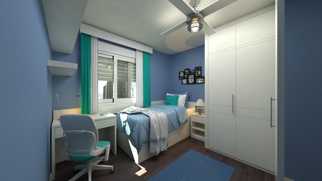 A blue dorm room with a bed on the wall by a window a built in closet and desk at the foot of the bed. 